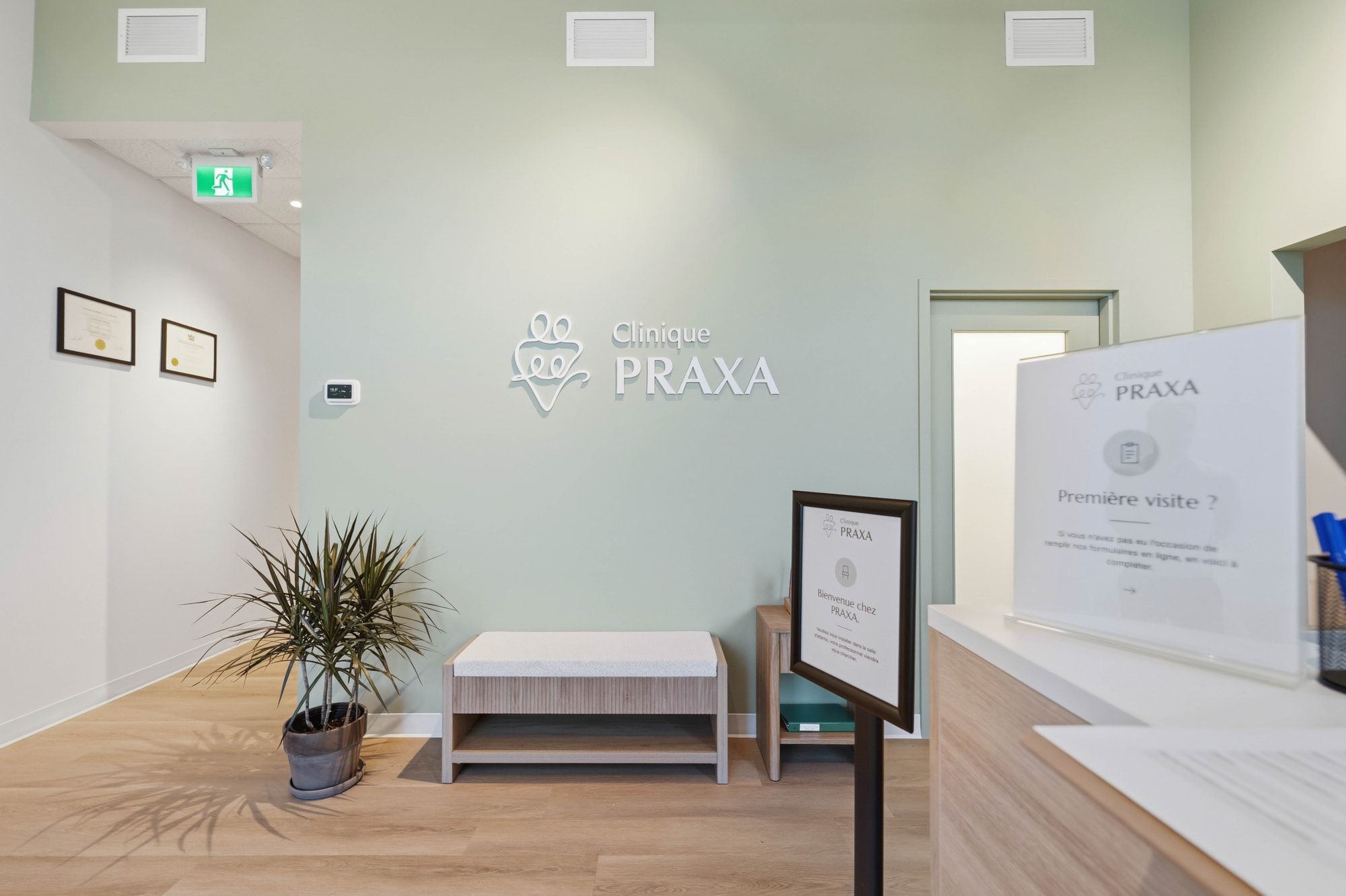 L’espace d’accueil de la Clinique PRAXA, avec son logo mural, un banc et une plante.